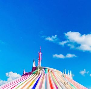 Space Mountain's iconic rainbow-striped dome peaks against a bright blue sky with white puffy clouds at Disney theme park.