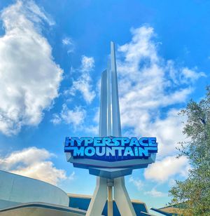 The iconic Hyperspace Mountain sign and spire against a bright blue sky with white fluffy clouds at Disneyland.