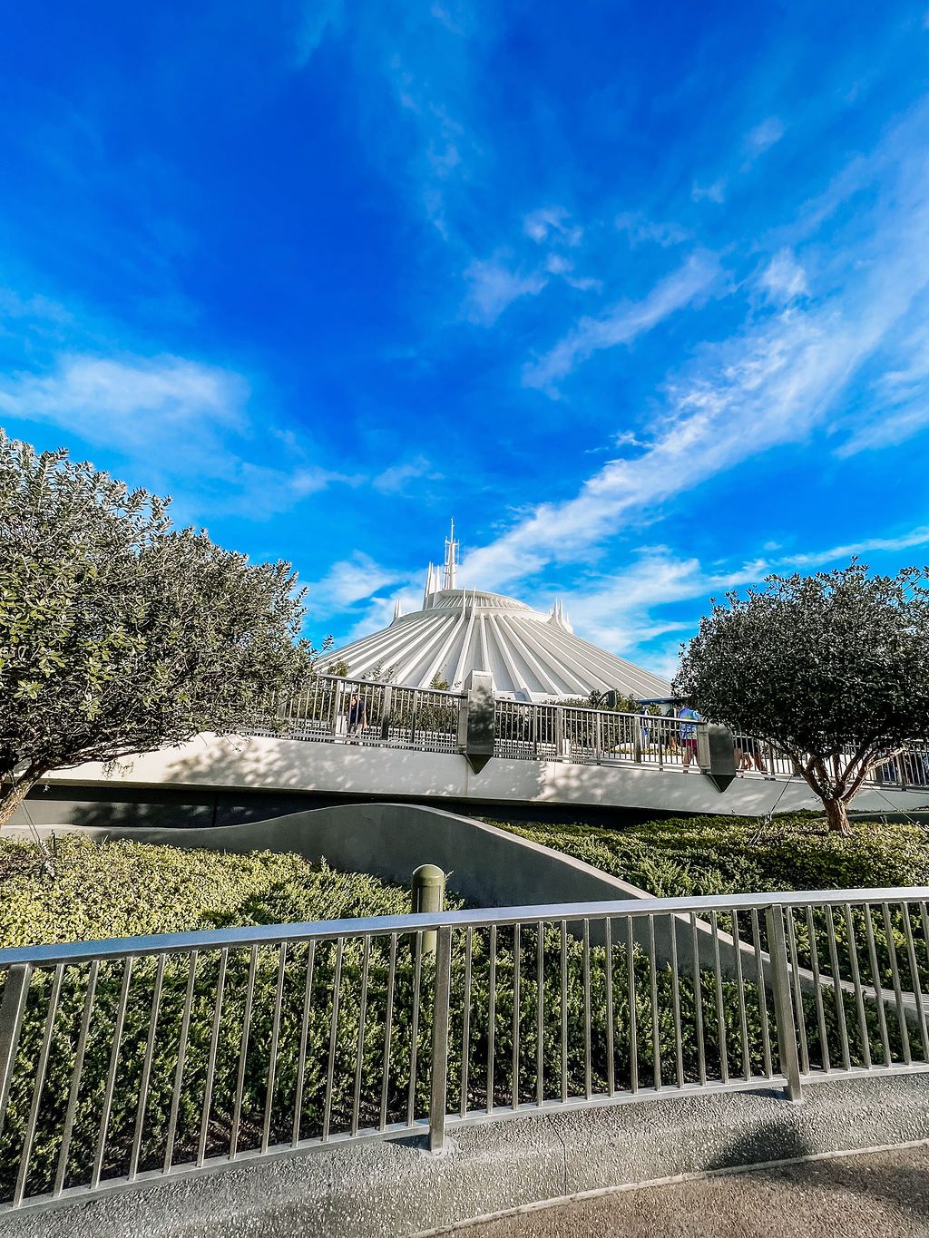 Panoramic view of Space Mountain at Disneyland Park against bright blue sky with white clouds and tropical landscaping.