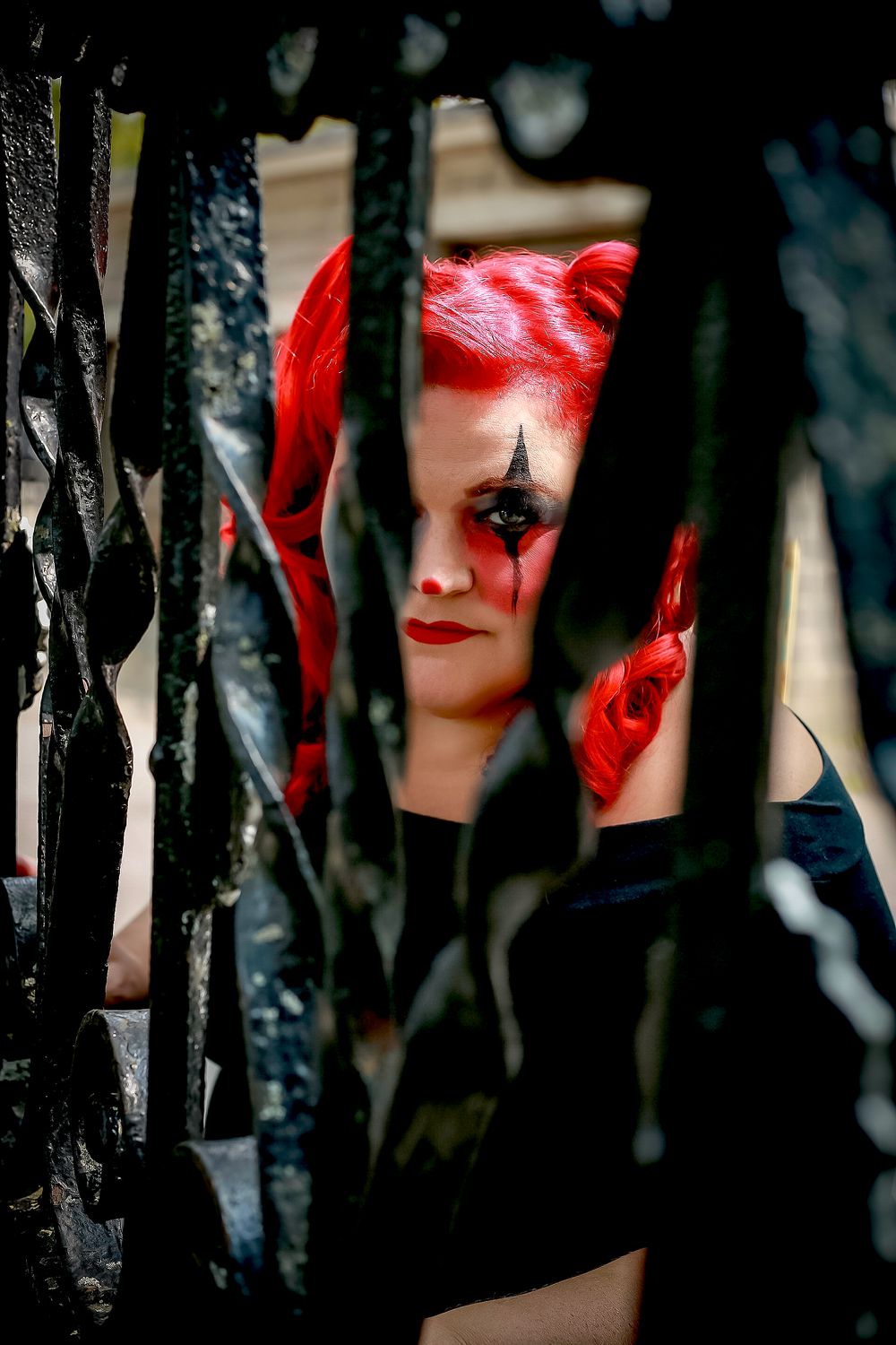 Dramatic portrait through iron bars showing red hair and dark gothic makeup.