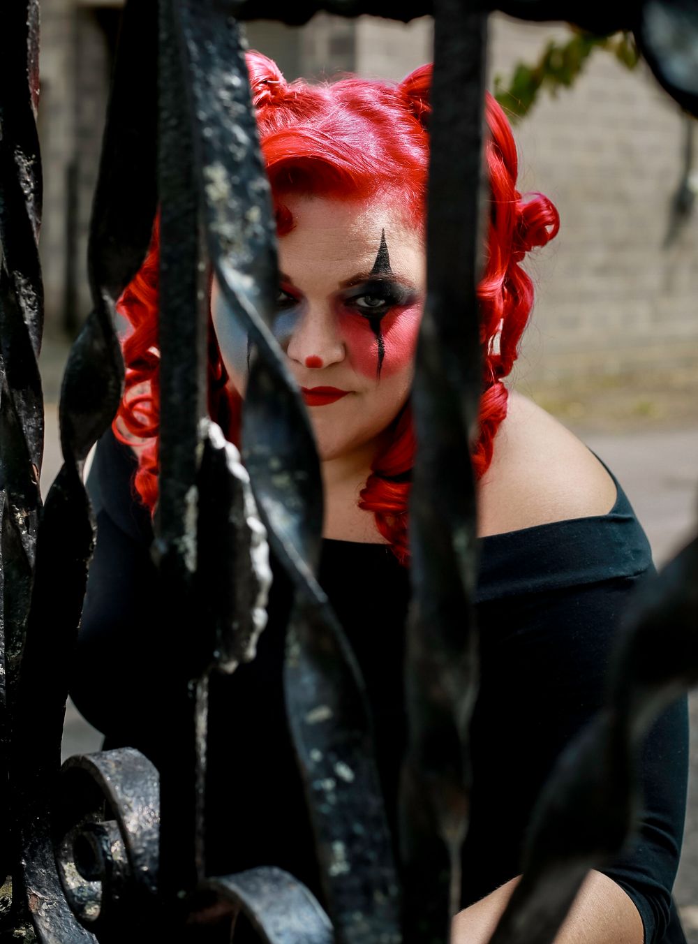 Gothic-style portrait through iron bars featuring dramatic red hair and dark makeup.