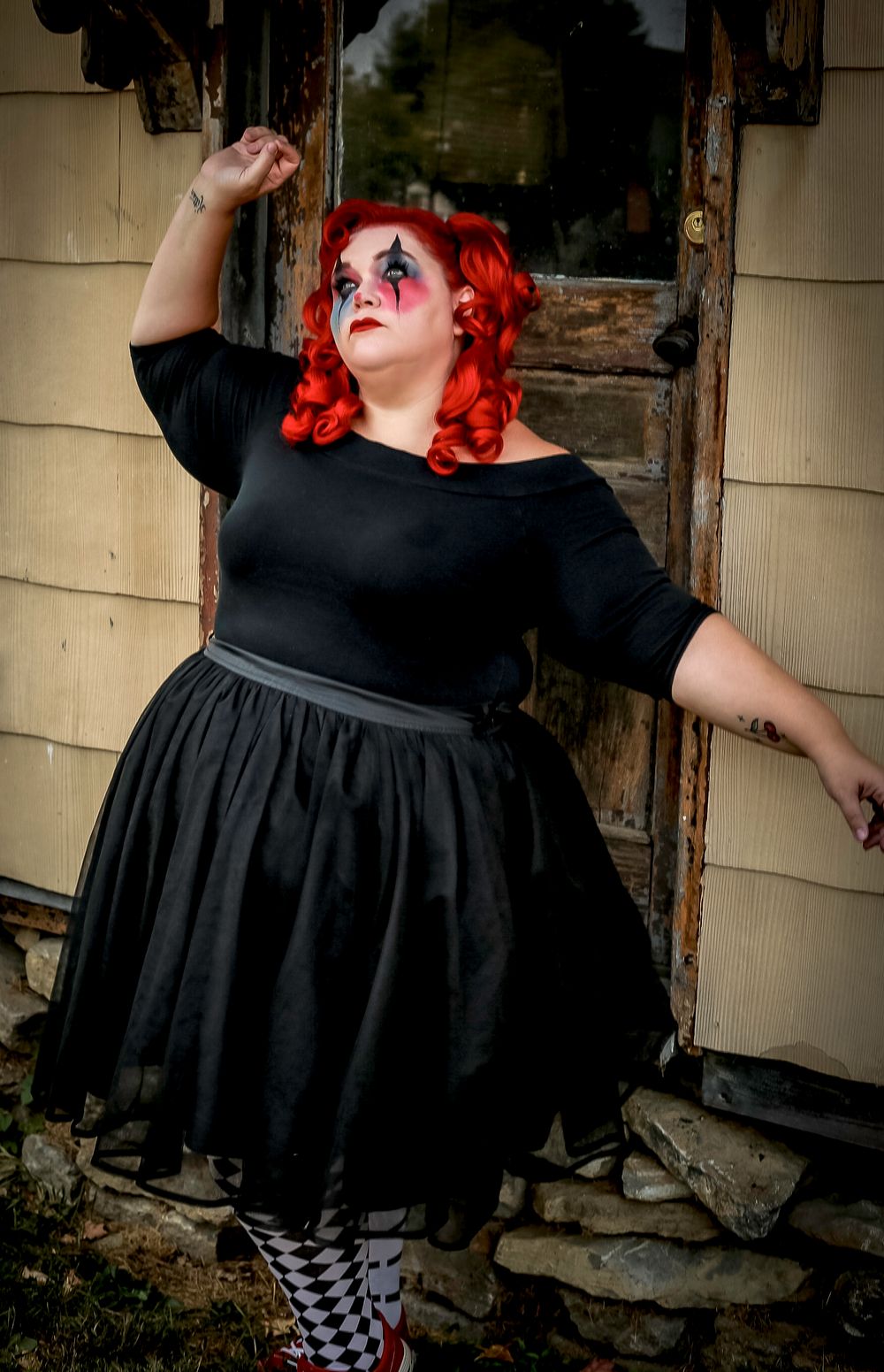 A figure in black dress strikes a dramatic pose against a weathered wall.