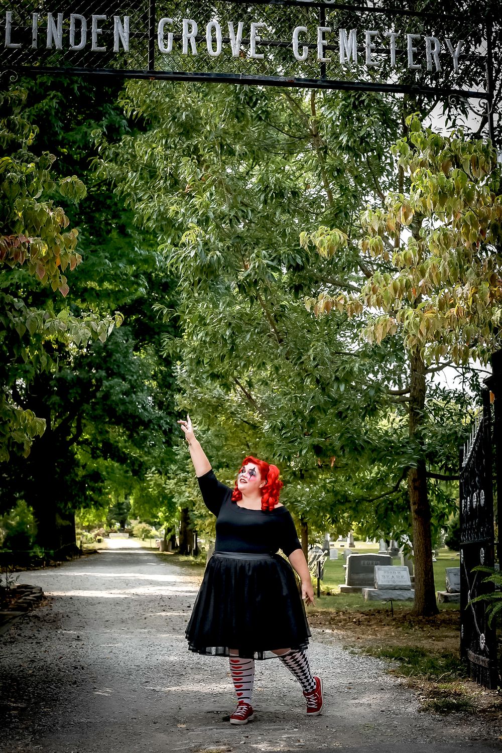 A gothic figure gestures dramatically under the Linden Grove Cemetery entrance sign.