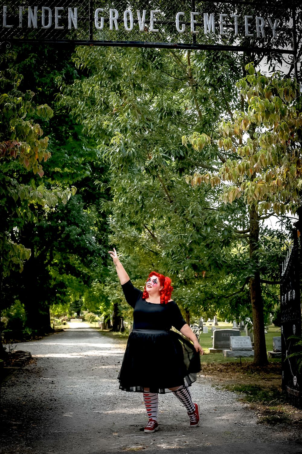 A dramatic pose under the Linden Grove Cemetery sign surrounded by green foliage.