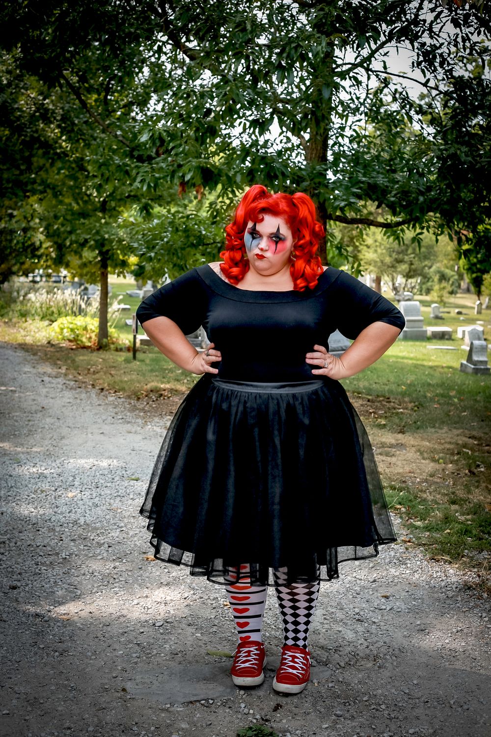 A figure in black dress and striped stockings poses confidently on a cemetery path.