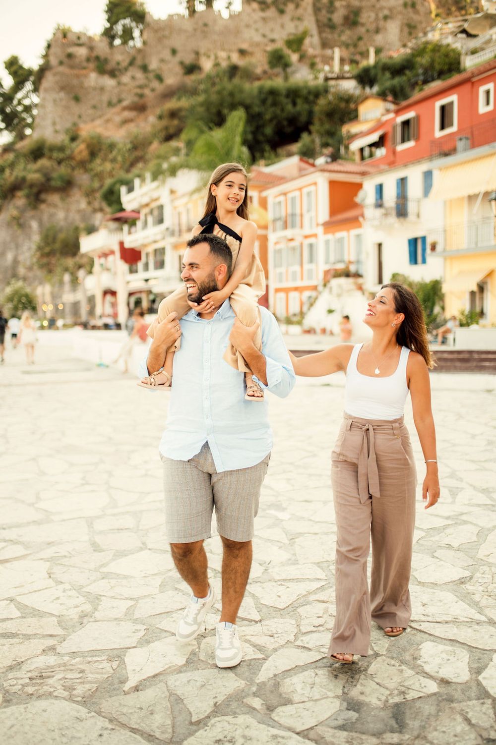 Family walking together on stone pavement with Mediterranean hillside architecture in the background.