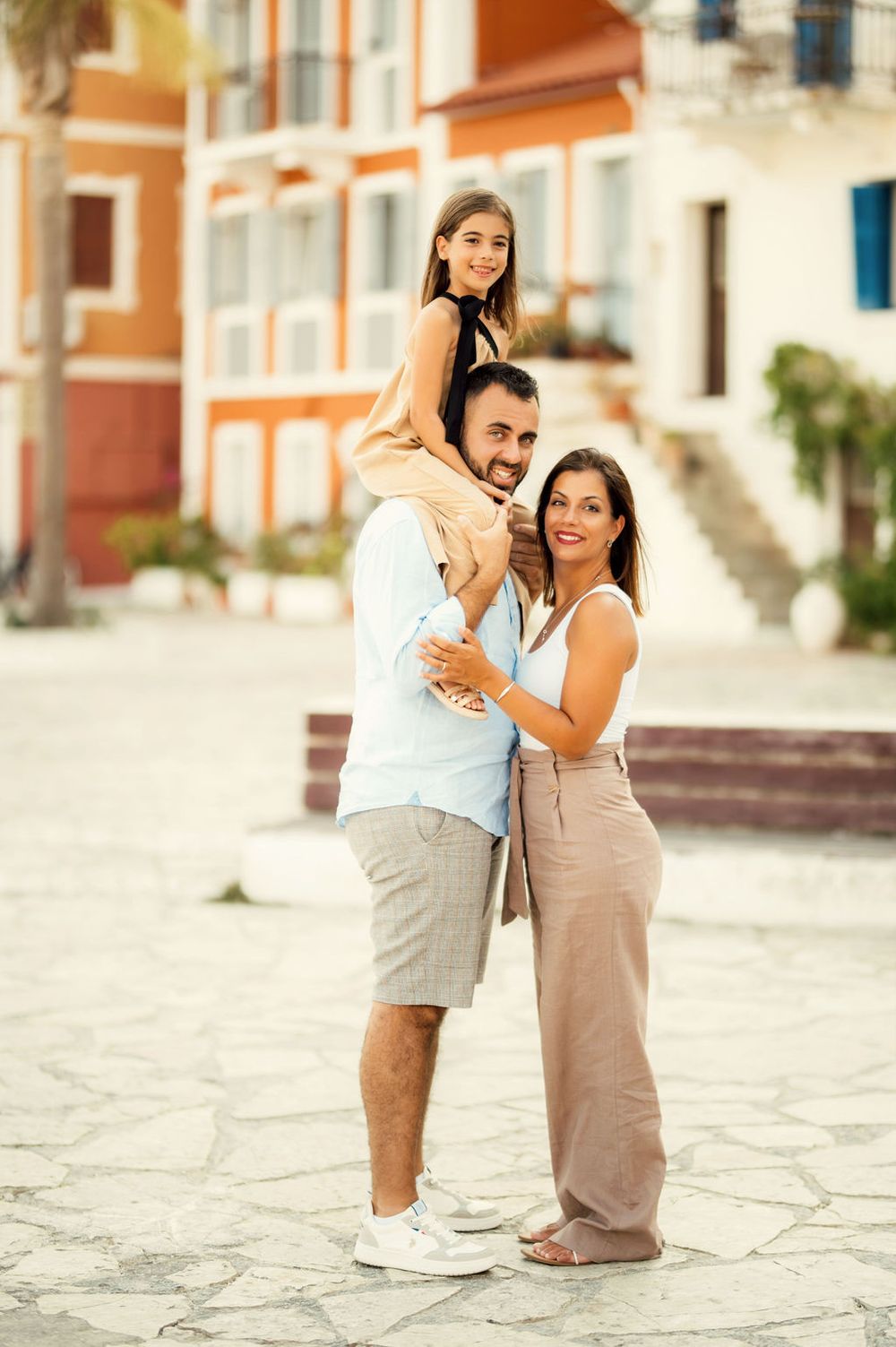 Three people pose together against a backdrop of sunny coastal buildings.