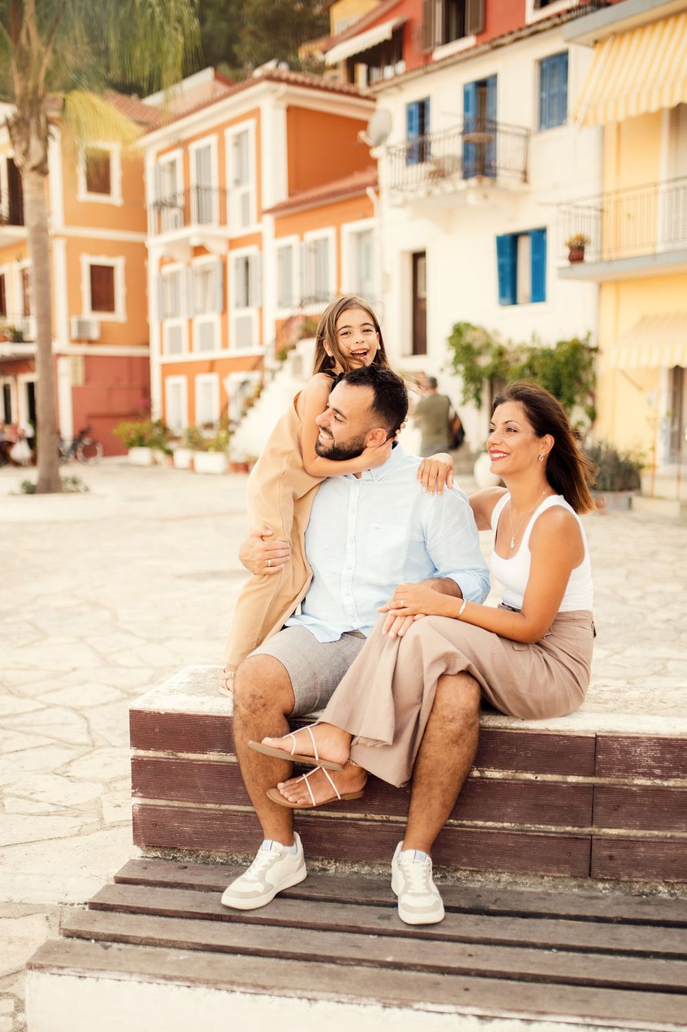 A family shares joyful moments on wooden steps against a backdrop of colorful Mediterranean buildings.