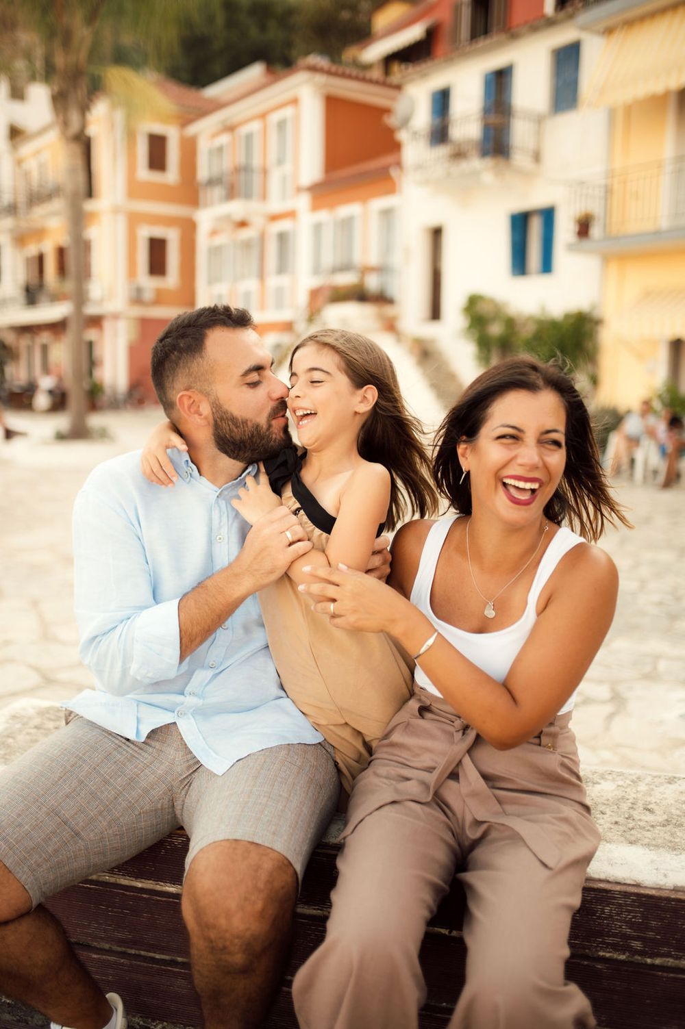 A happy trio shares laughter while sitting on wooden steps in a Mediterranean coastal town.