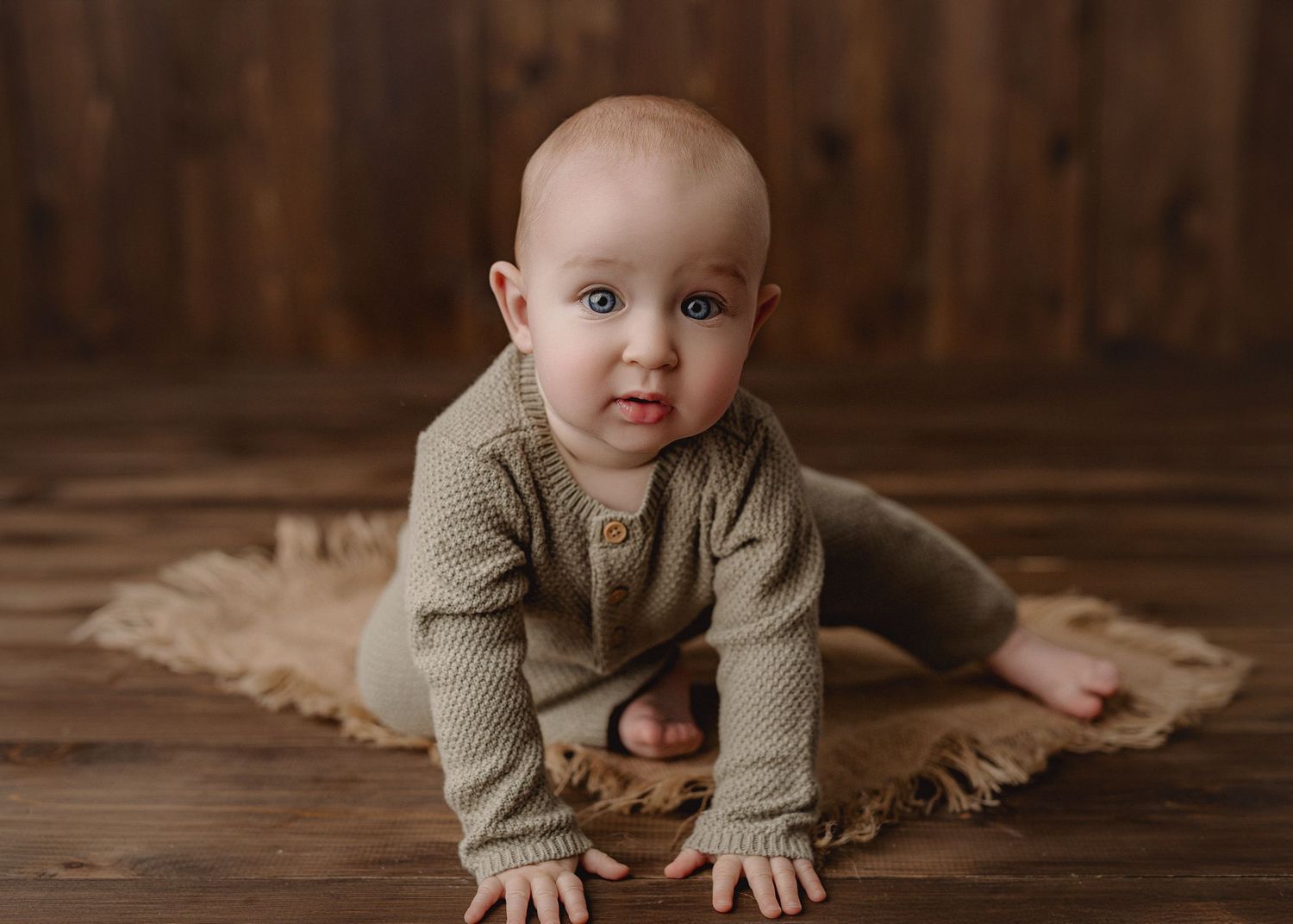 Small child sits in a woven tan macrame basket against a white wooden backdrop on soft beige fabric.