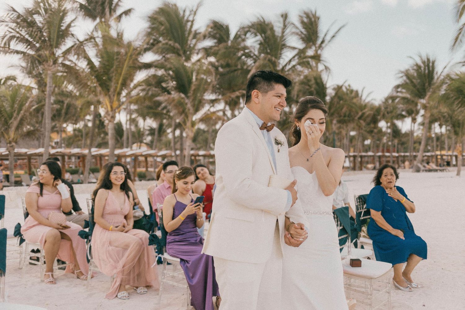 Beach wedding celebration with palm trees and guests enjoying the tropical setting.