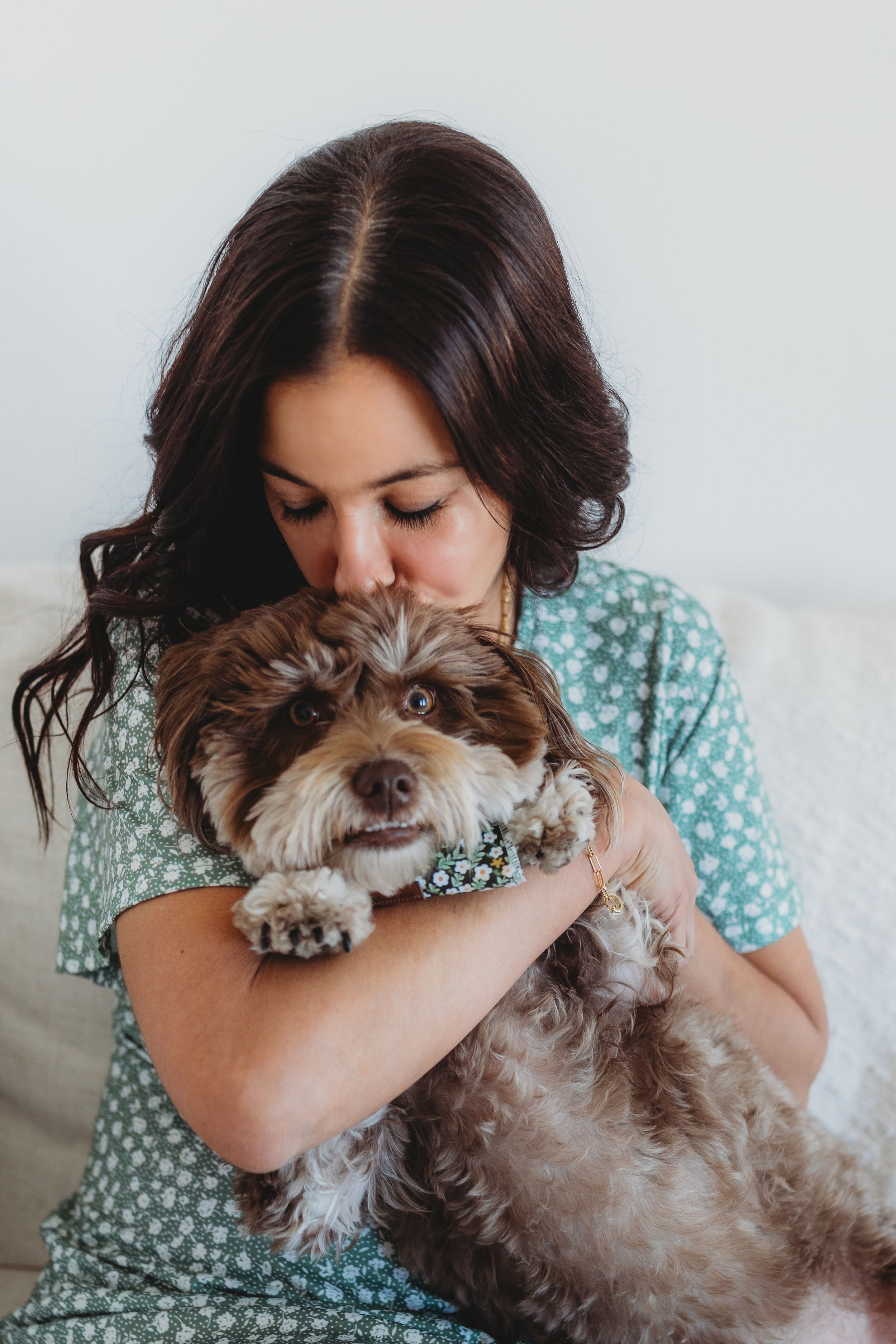 Person in blue polka dot dress cuddles brown and white mixed breed dog while relaxing at home.