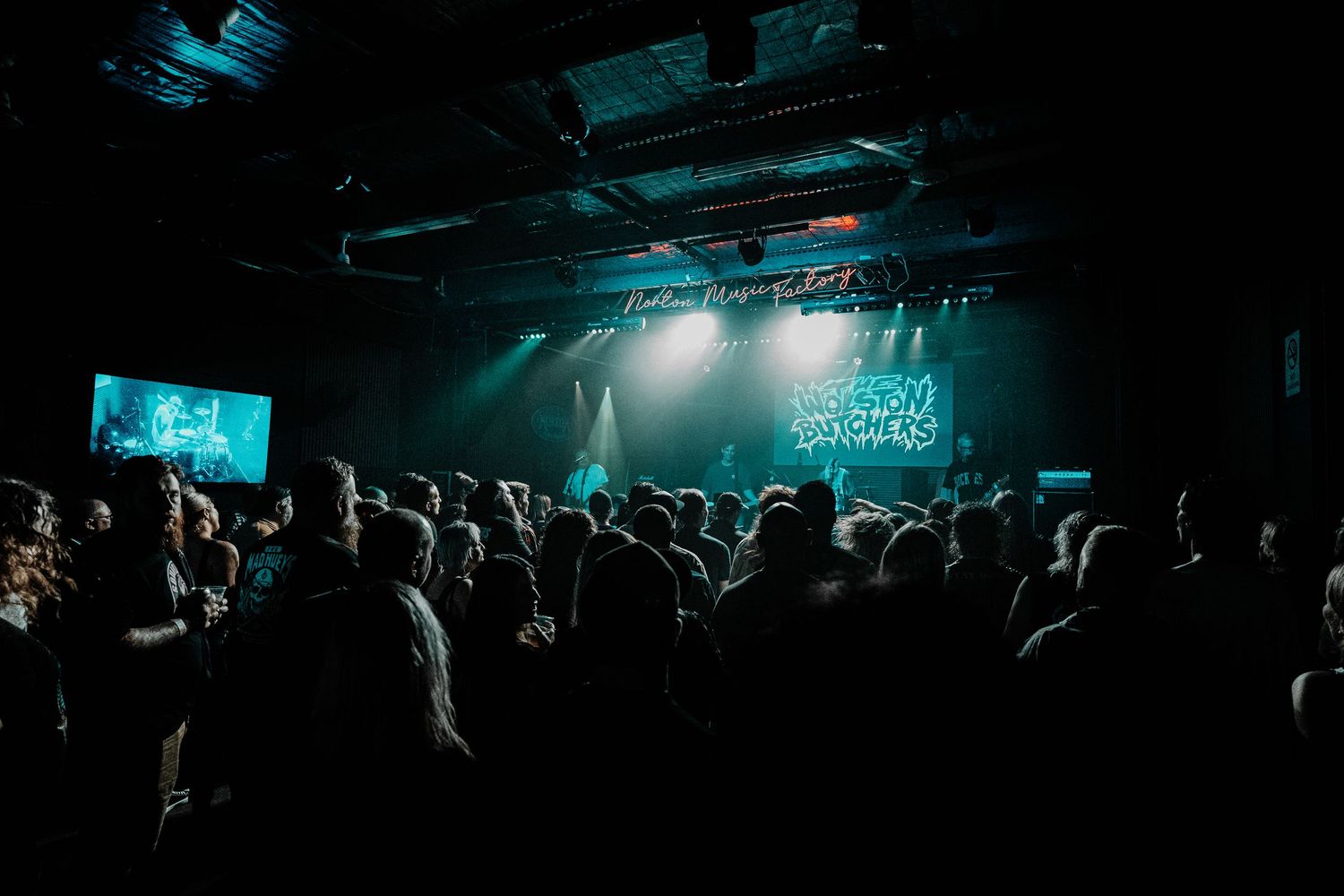 Silhouetted crowd at a concert venue with moody blue lighting and stage illumination in the background.