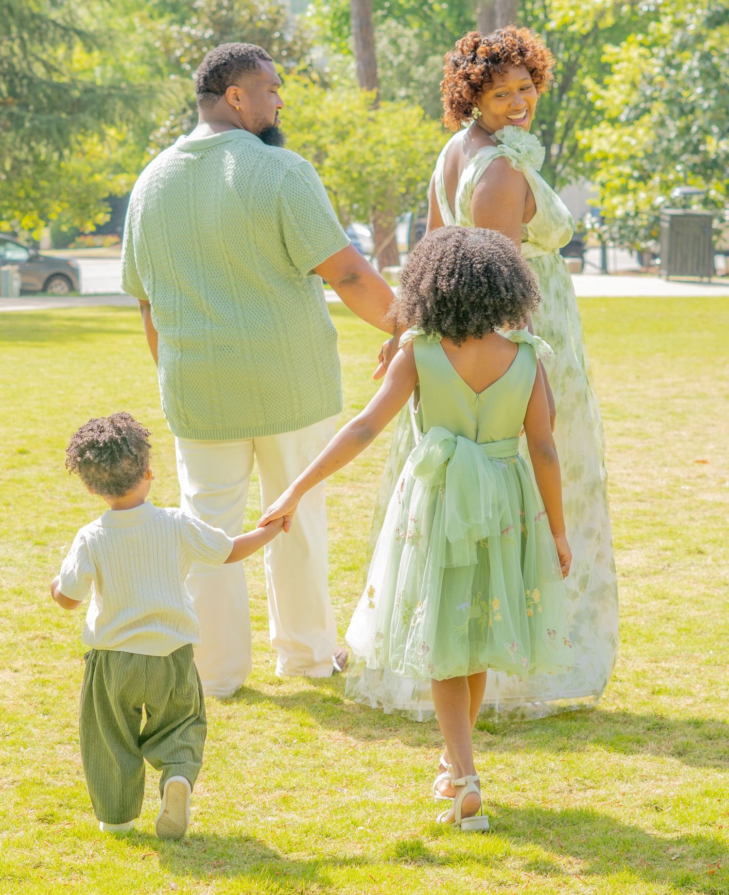 A family in coordinated mint green and white outfits walks together on a sunny lawn during a formal occasion.