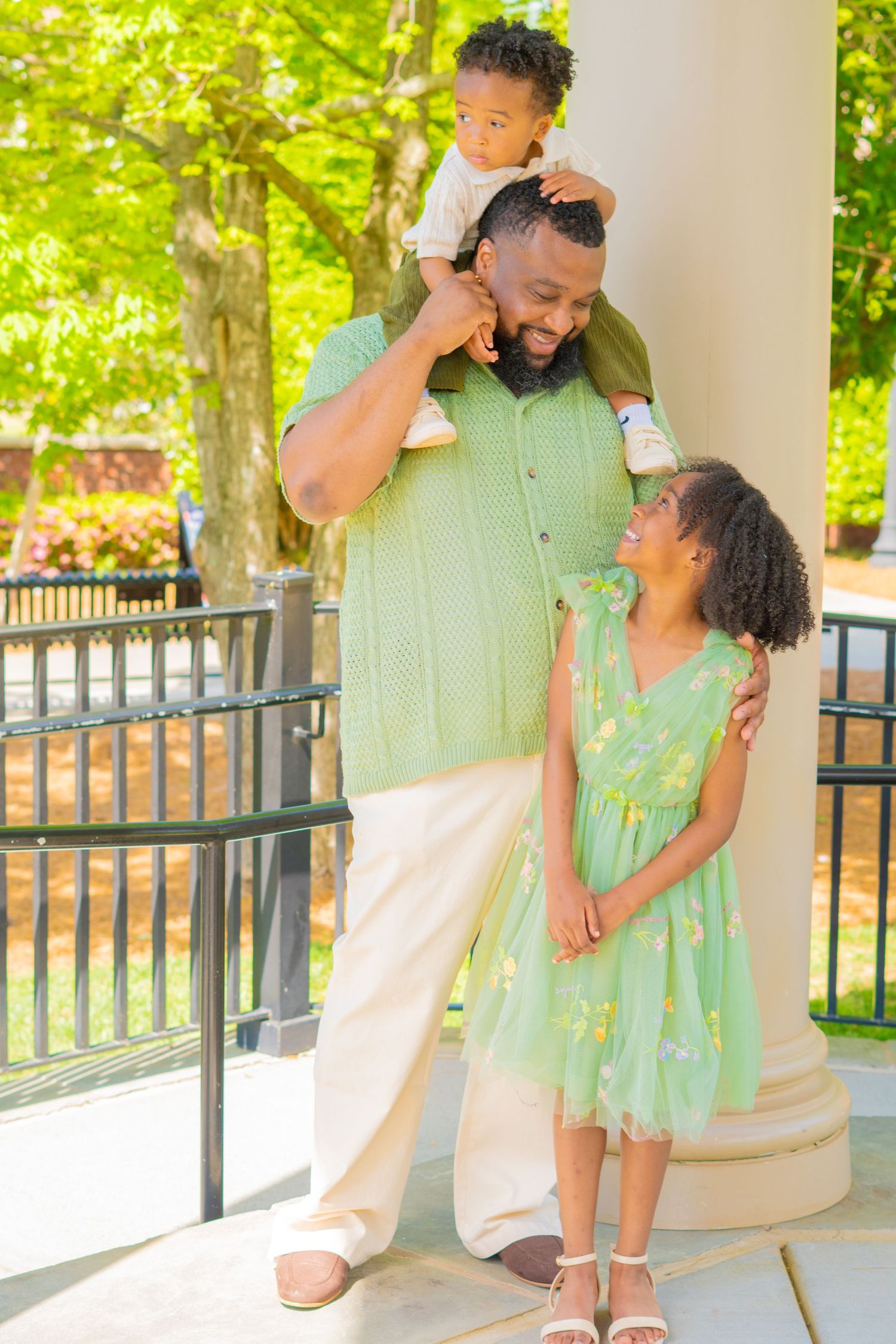 A joyful family wearing coordinating mint green outfits poses together on a porch with white columns.
