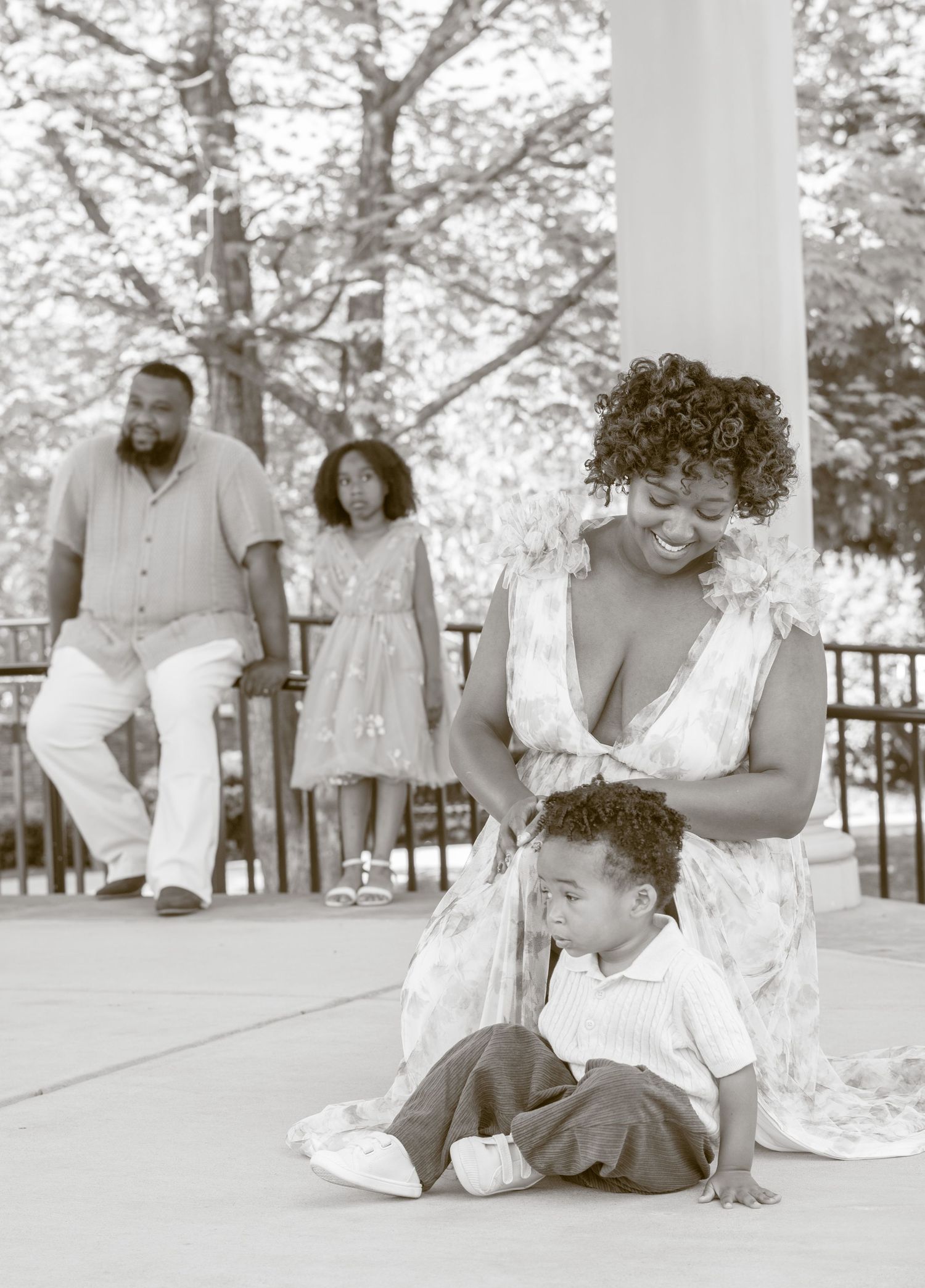 Black and white photograph showing a loving family moment on a porch with trees in the background.