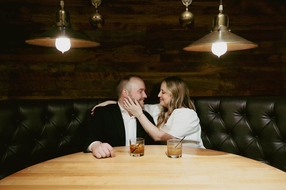 Two people share an intimate moment at a restaurant booth under pendant lighting.