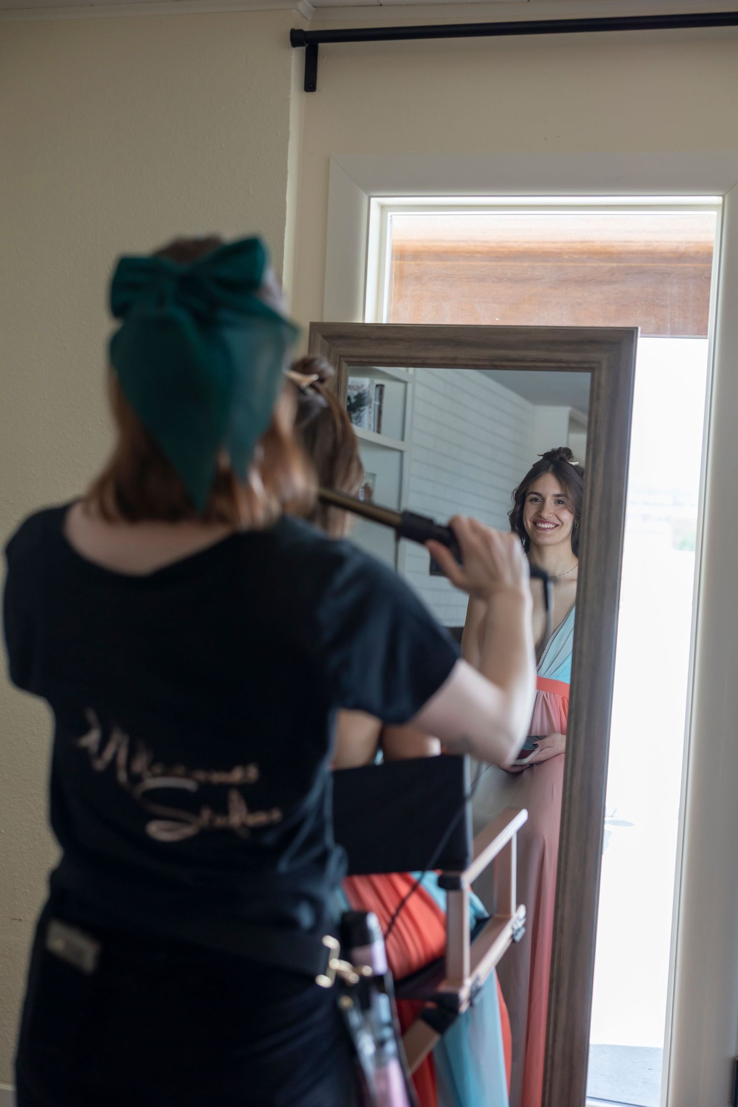 client looking in mirror with hair stylist curling hair
