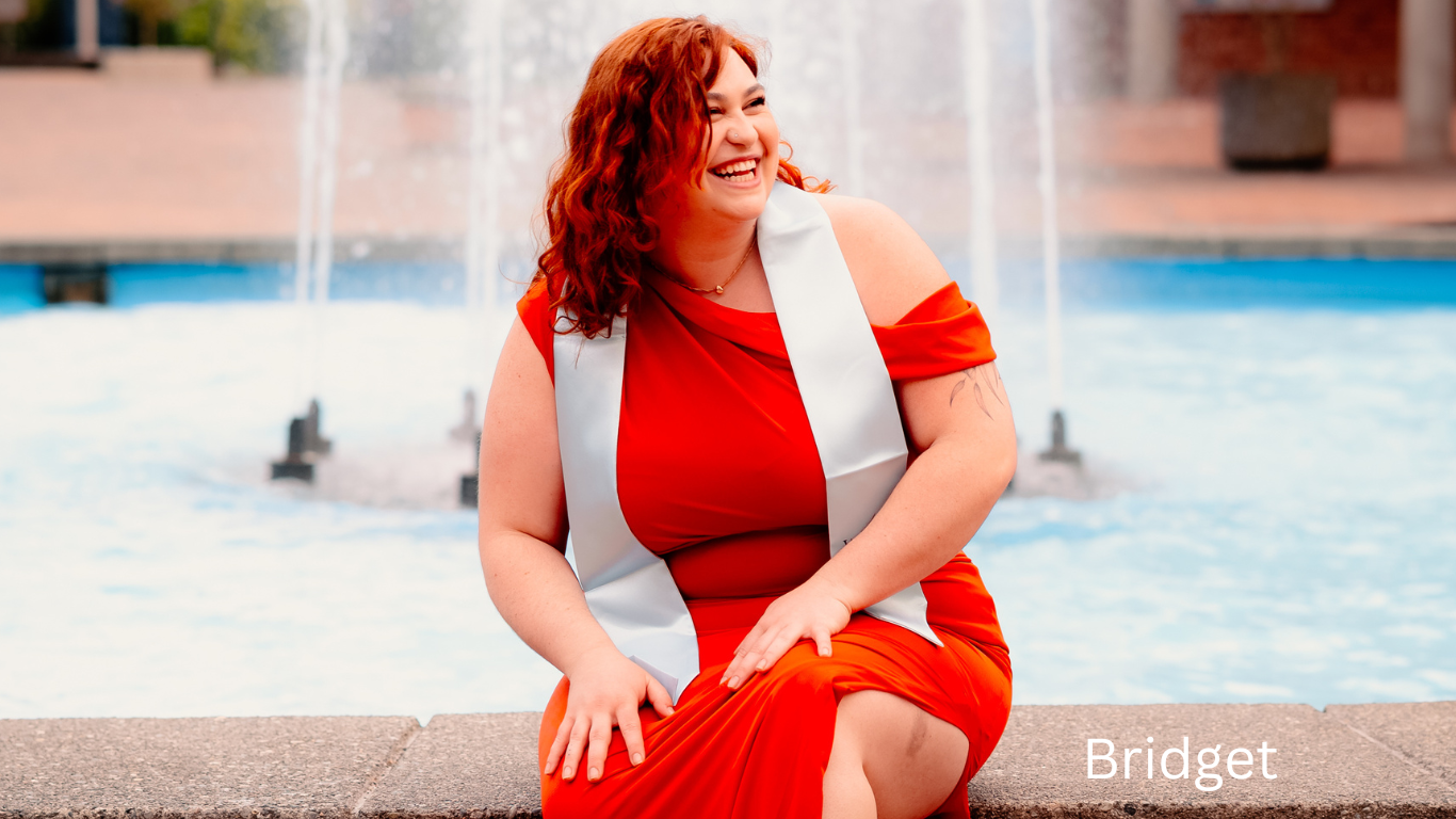 Someone in red dress sitting by fountain edge on sunny day.