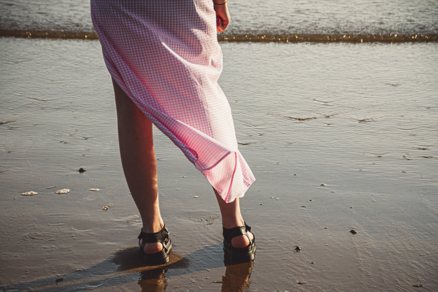 Aesthetic dreamy photograph image showing a female from behind and from the hips down, standing on the edge of the sea shore.