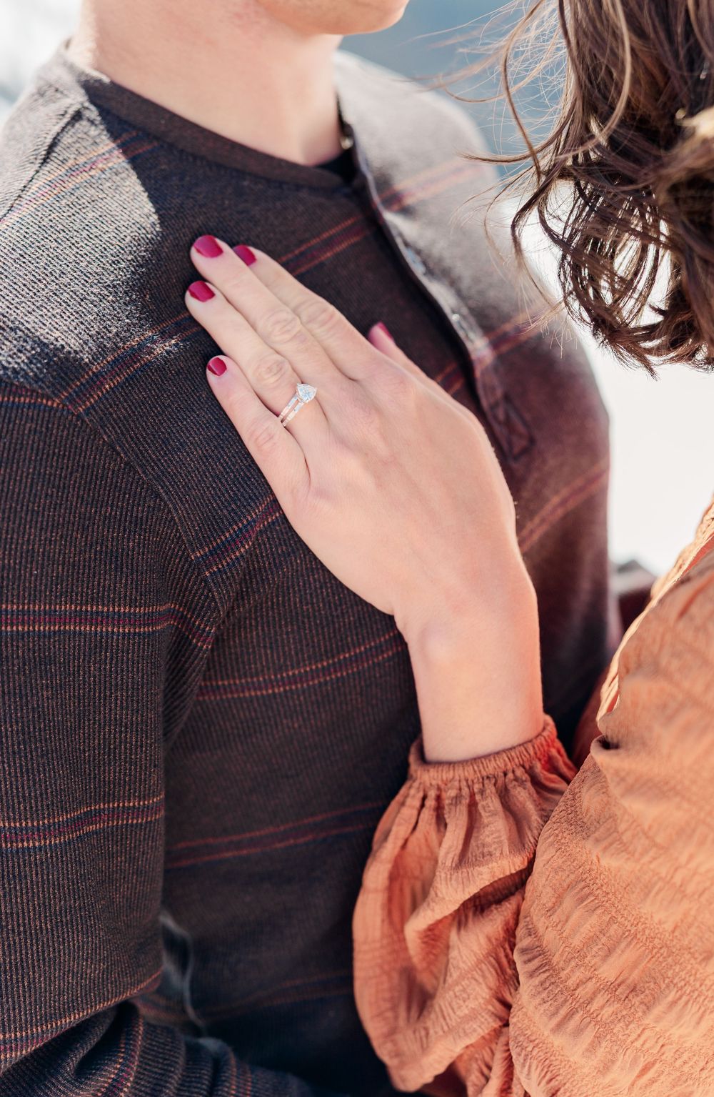 Close-up of newly engaged person showing off diamond ring while wearing burgundy sweater and rust-colored sleeve.