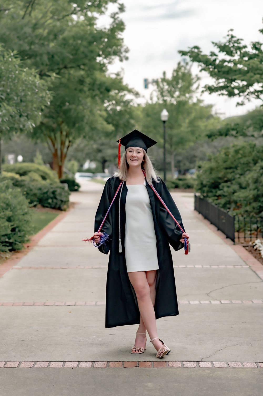 Graduate poses on campus walkway wearing traditional black graduation regalia.