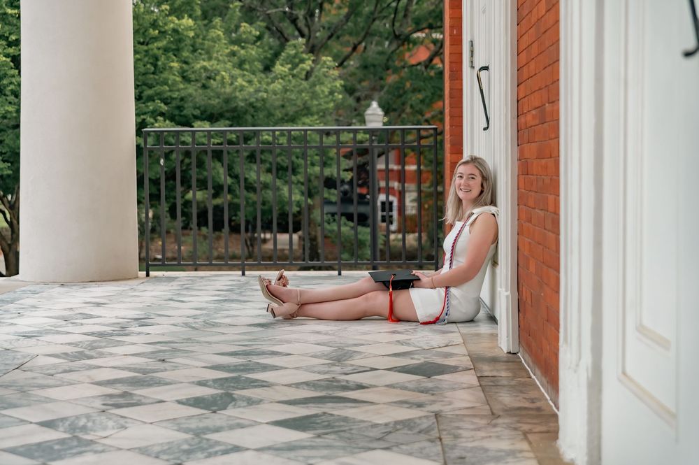 Graduate sitting casually on marble floor with graduation cap and gown.