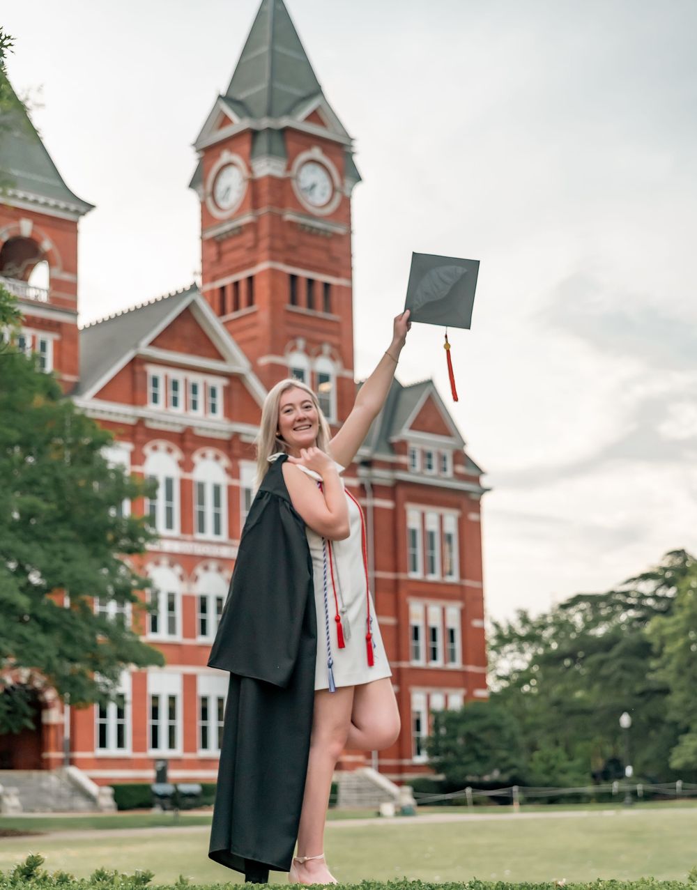 Graduate celebrating in front of red brick clock tower building.