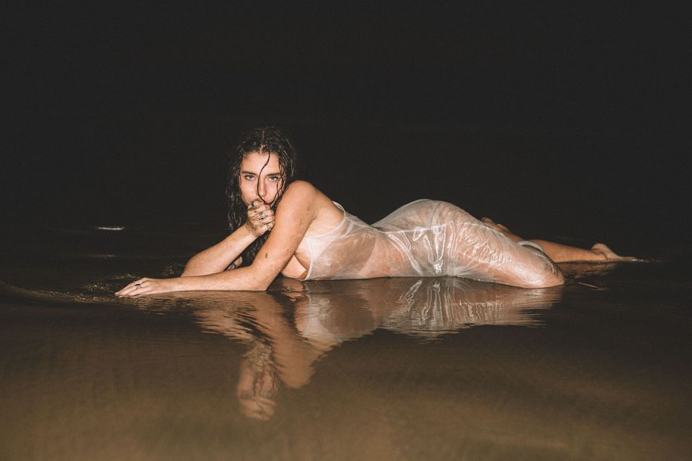 Person in shimmering dress lying in shallow water at night creating reflective effect.