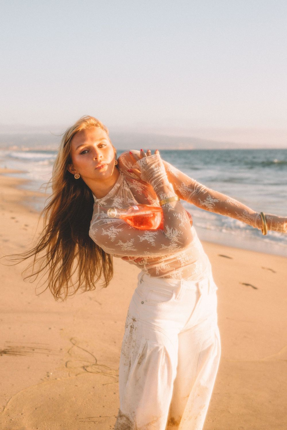 Person in white outfit dances on beach with hair flowing in the wind.