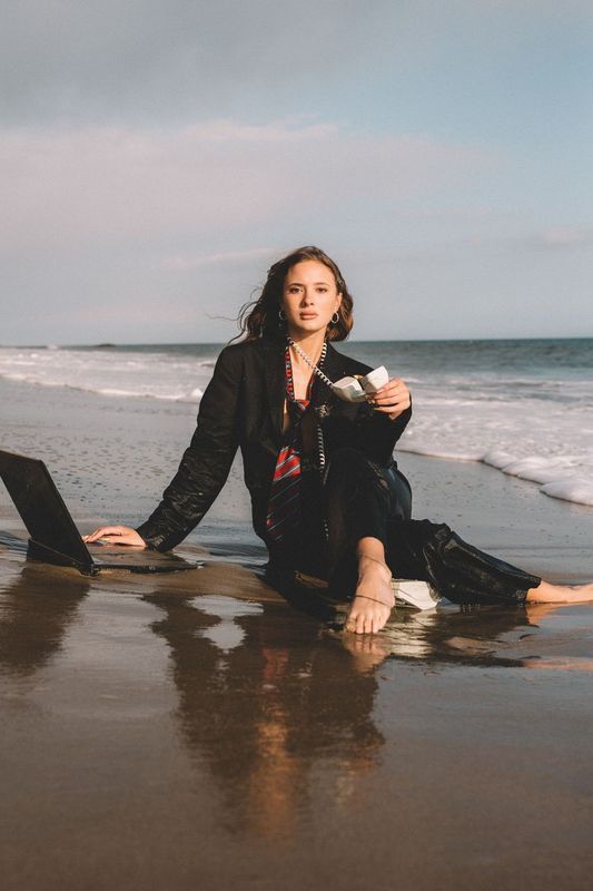 Person sits with laptop on beach shore during overcast day.