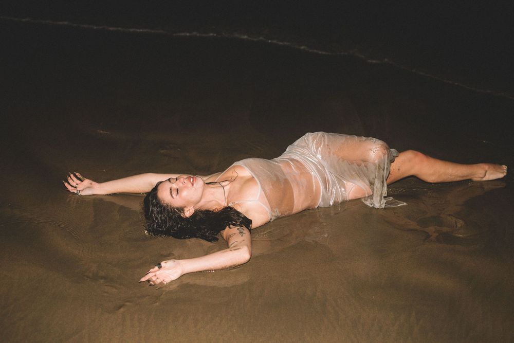 Figure in light colored dress lying in shallow ocean water at dusk.