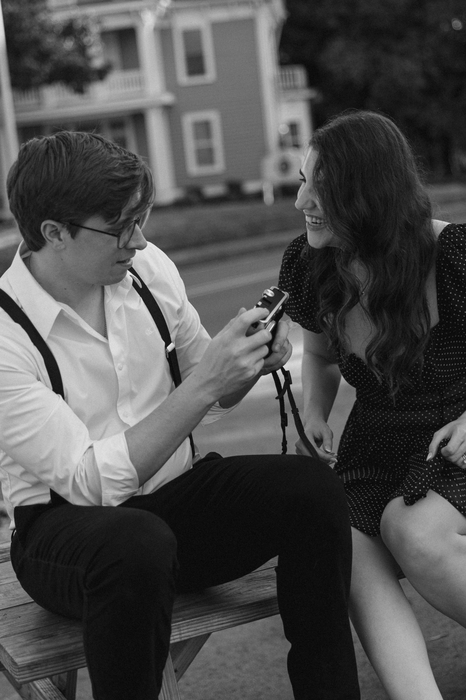 A couple sitting on a bench sharing a moment while looking at a mobile phone in black and white photography.