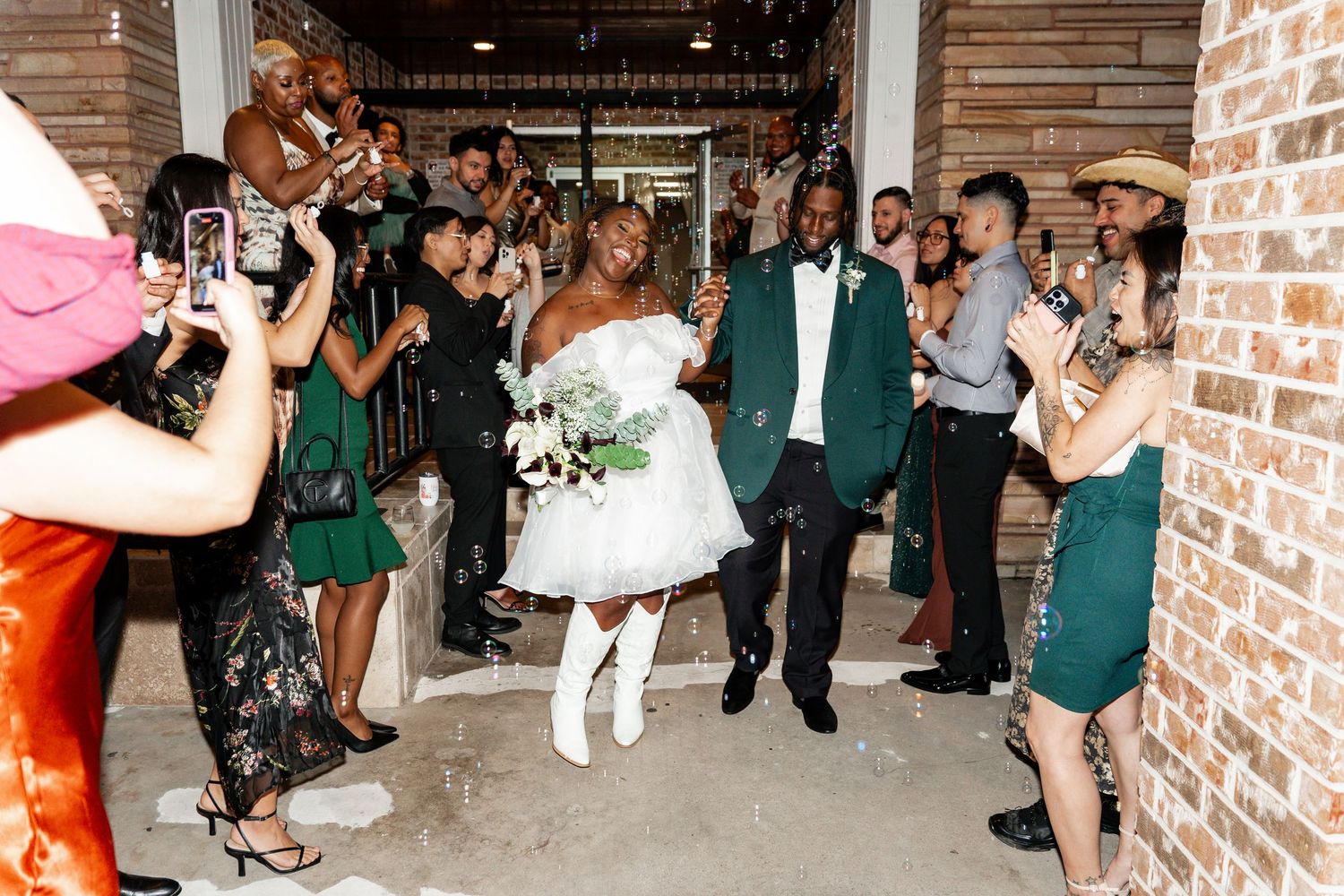 A happy couple embraces and laughs together while surrounded by green foliage outdoors.