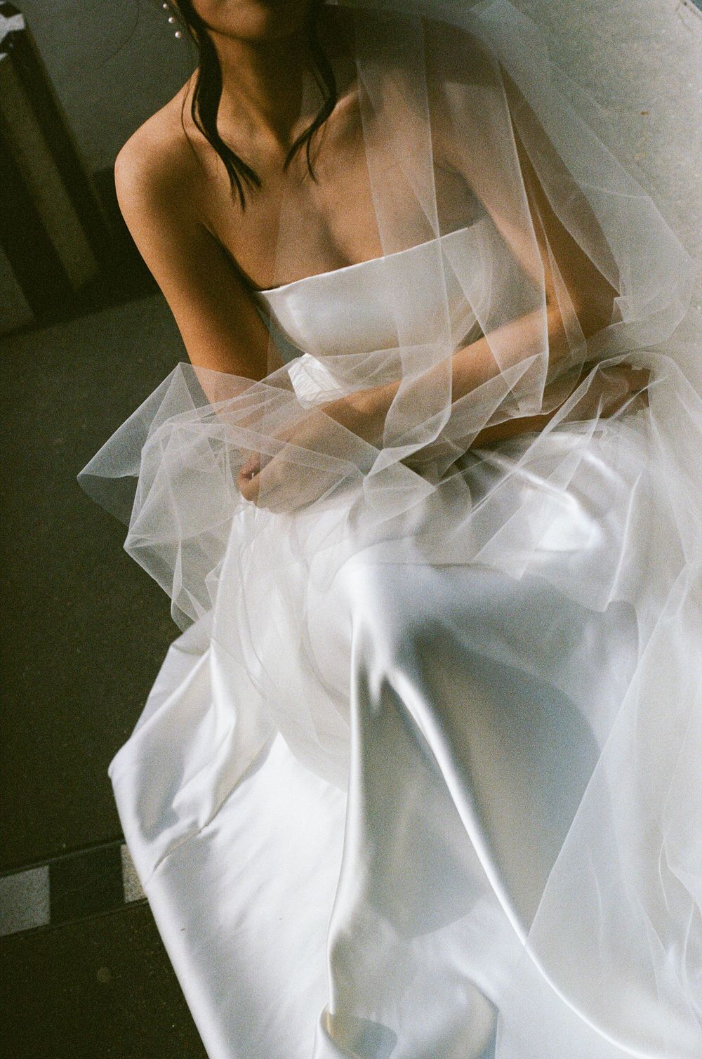 A bride in a white strapless gown sits gracefully draped in delicate layers of tulle veil.