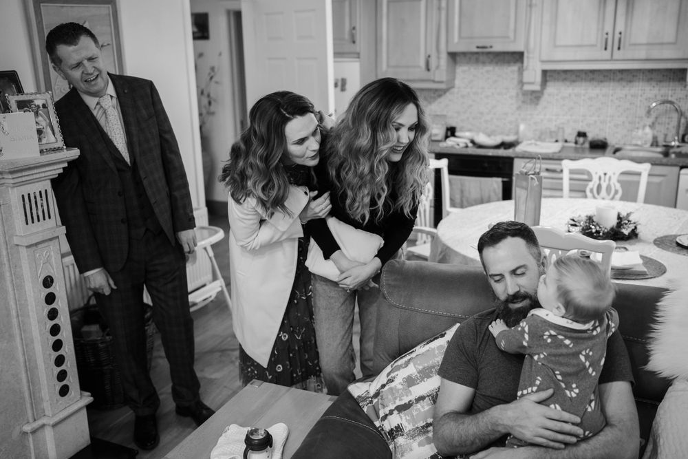 Black and white candid family moment in a kitchen with people gathered around and laughing.