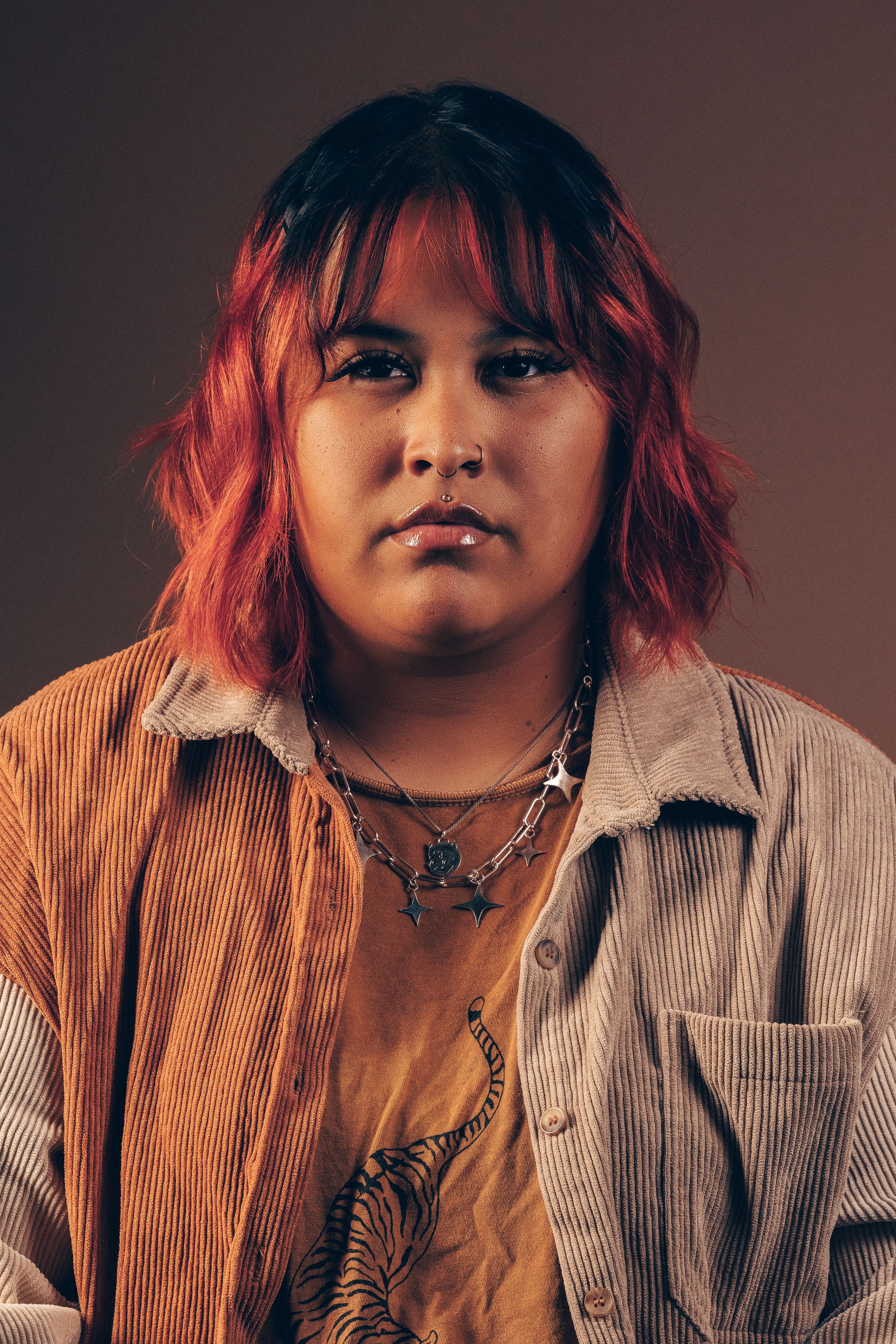 Studio portrait series featuring warm lighting and red-dyed hair with a corduroy button-up shirt.