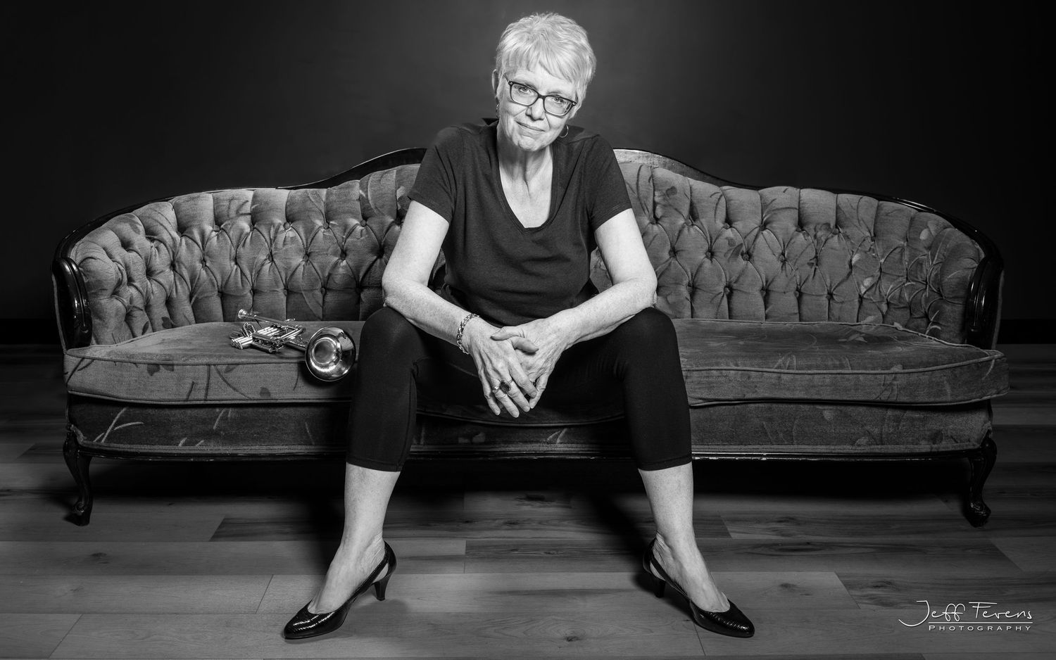 A Black & White Image of a woman sitting on a couch. With a trumpet on her right side. Jeff Fevens Photography in Fredericton, New Brunswick