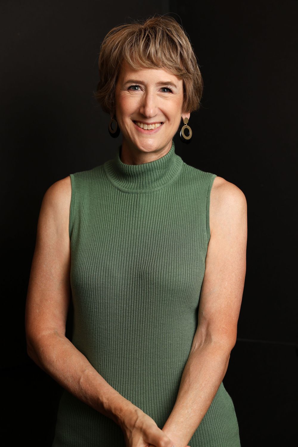 Portrait of a person wearing a green sleeveless turtleneck against dark background.