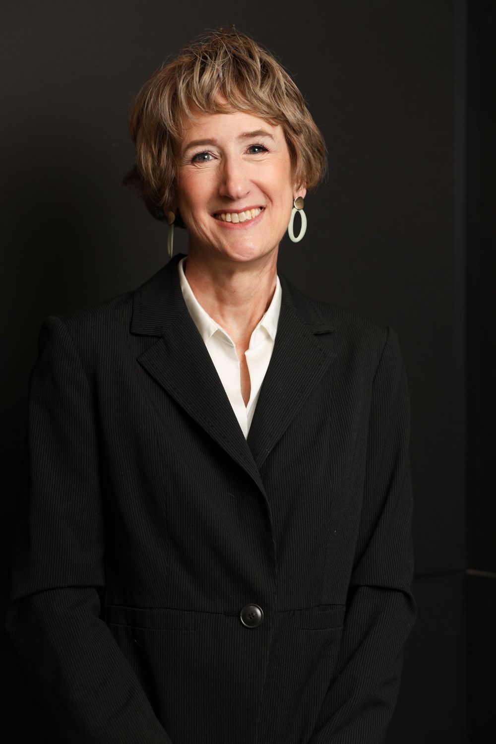 Business portrait of a person in black suit jacket and white shirt with bright jewelry.
