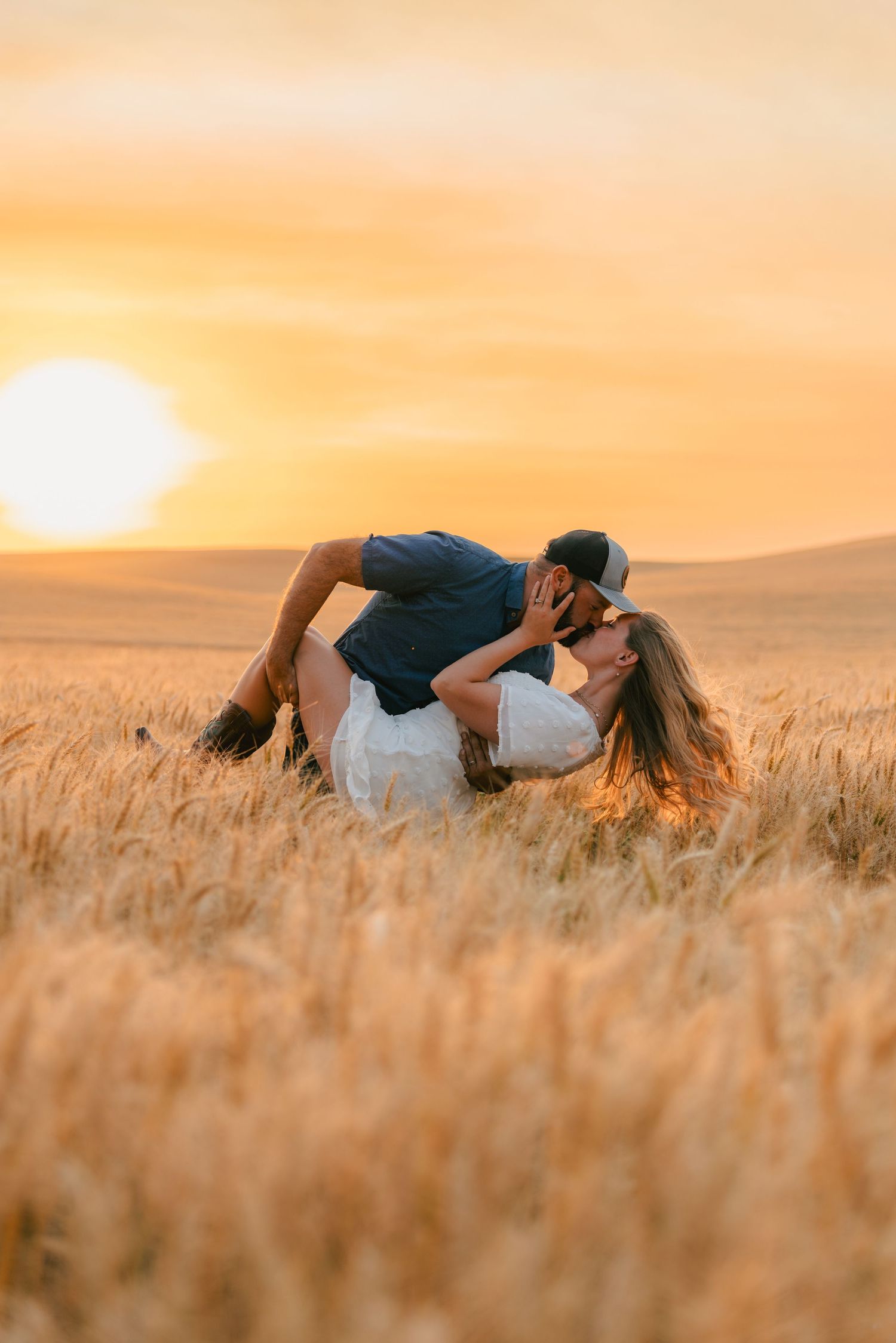 A couple in black shirts and jeans poses together at the beach during sunset with ocean waves in the background.