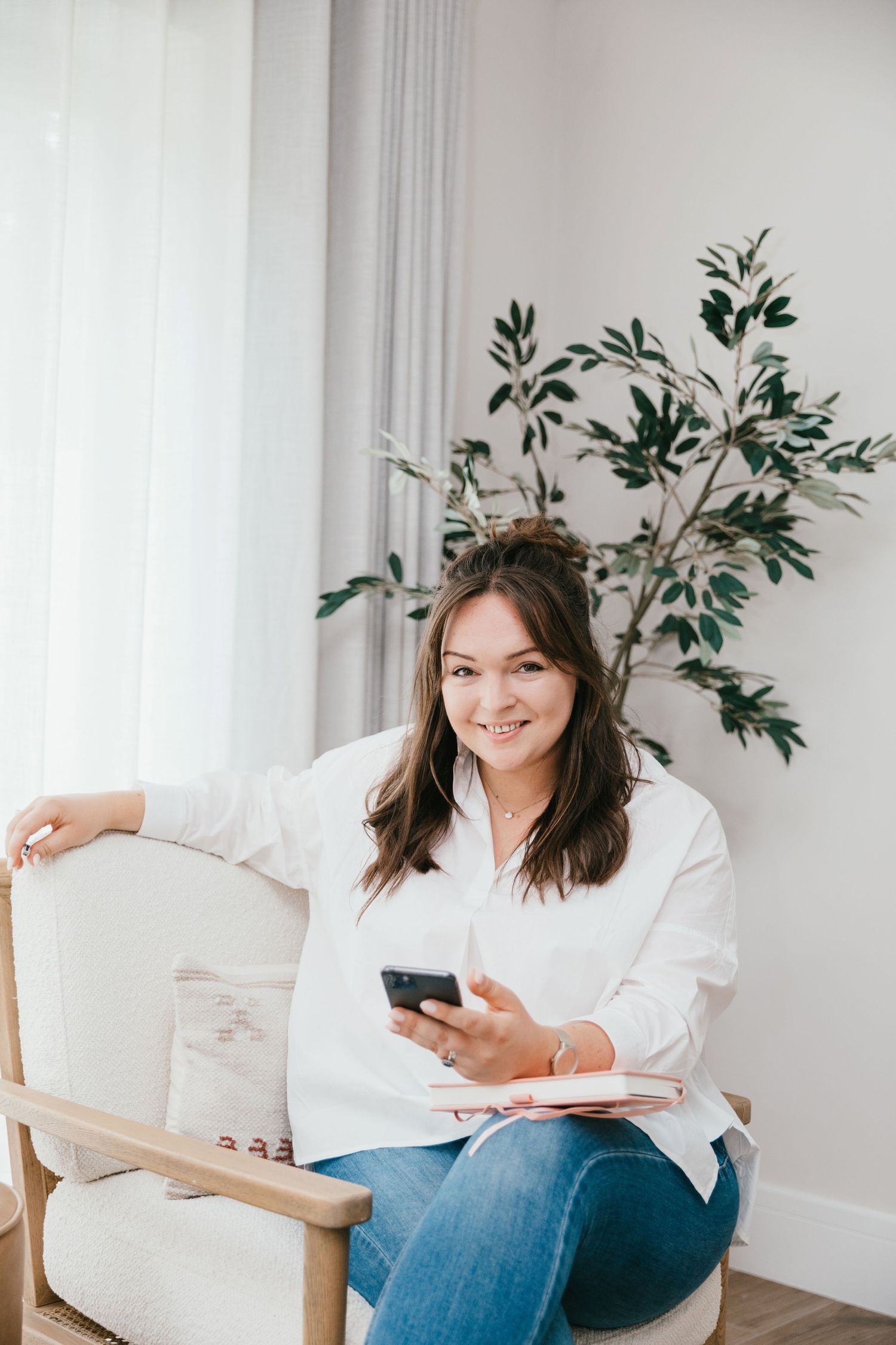 photo of photographer Katie Rhona Photography in white shirt and jeans with phone in hand smiling whilst seated.