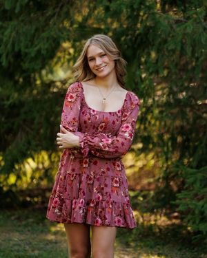 A person in a floral maxi dress poses outdoors in a garden setting during golden hour lighting.