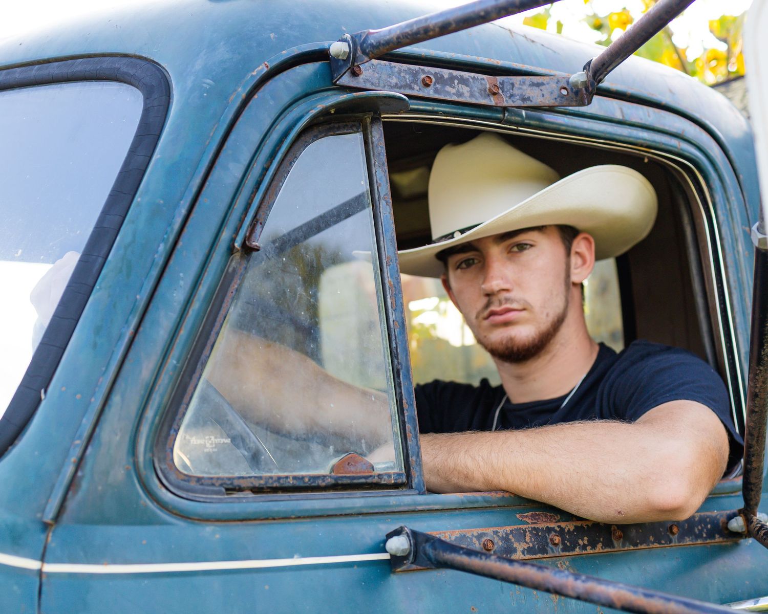 Turquoise vintage pickup truck with cowboy in white hat sitting in driver's seat.
