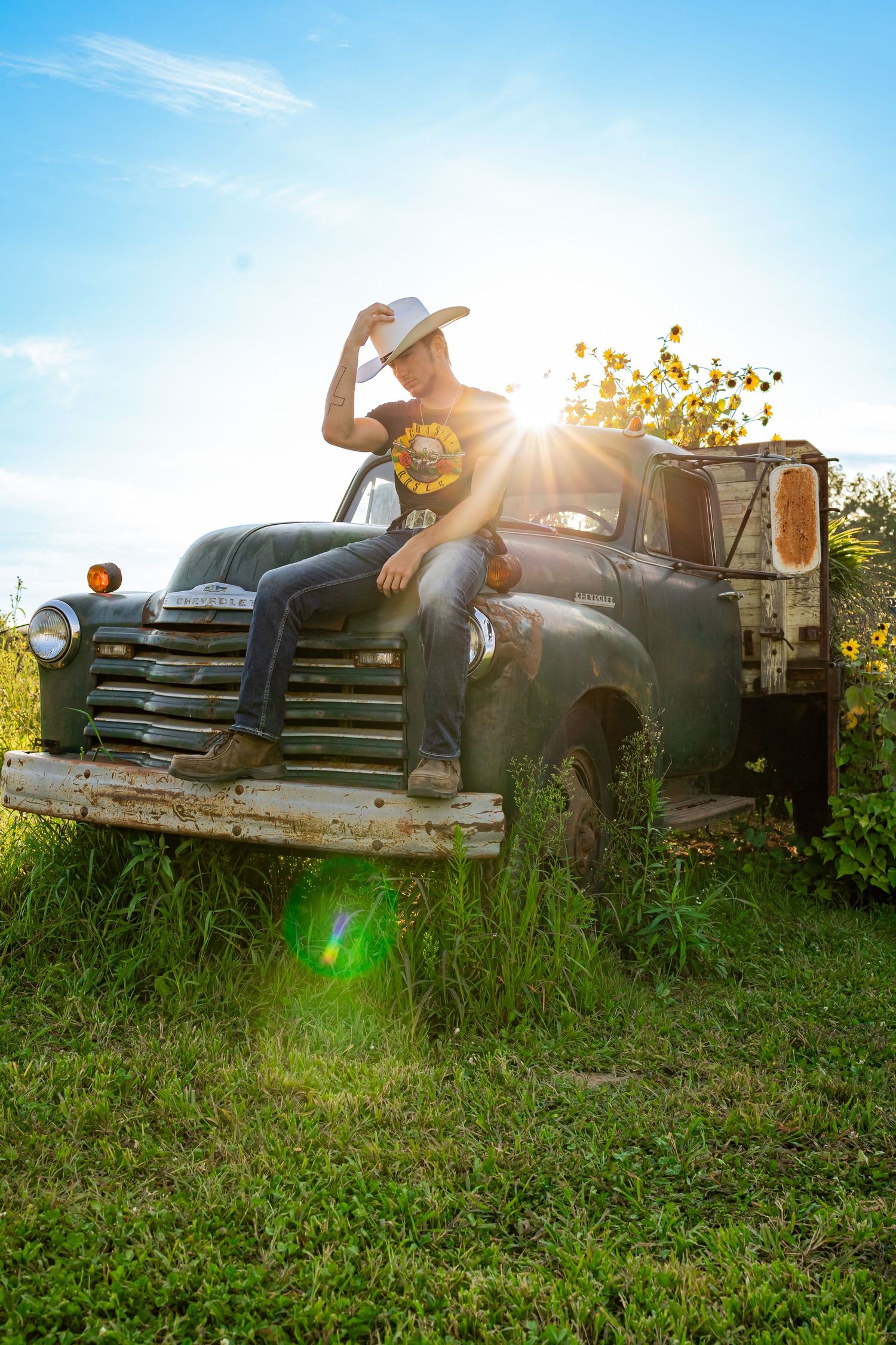 Vintage rustic truck in a sunny field with wildflowers and sun flare creating a dreamy summer scene.