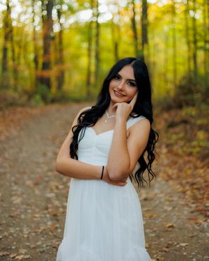 Woman in white dress poses gracefully among autumn leaves on forest path during fall photoshoot.