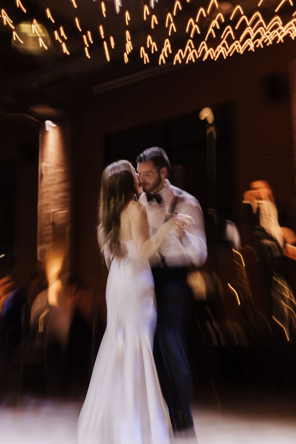 A couple shares their first dance at a wedding reception under twinkling lights in a dark romantic venue.