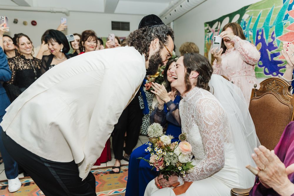 A joyful celebration at an indoor wedding ceremony with people wearing white outfits during a special moment.