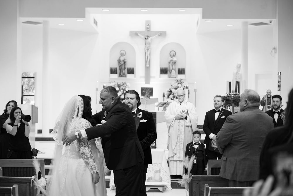 Black and white photograph of a traditional Catholic wedding ceremony taking place inside a church sanctuary with crucifix visible.