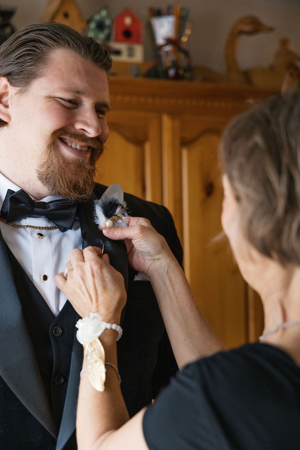 Someone helps adjust a black bow tie on a formal tuxedo while getting ready for a special occasion.